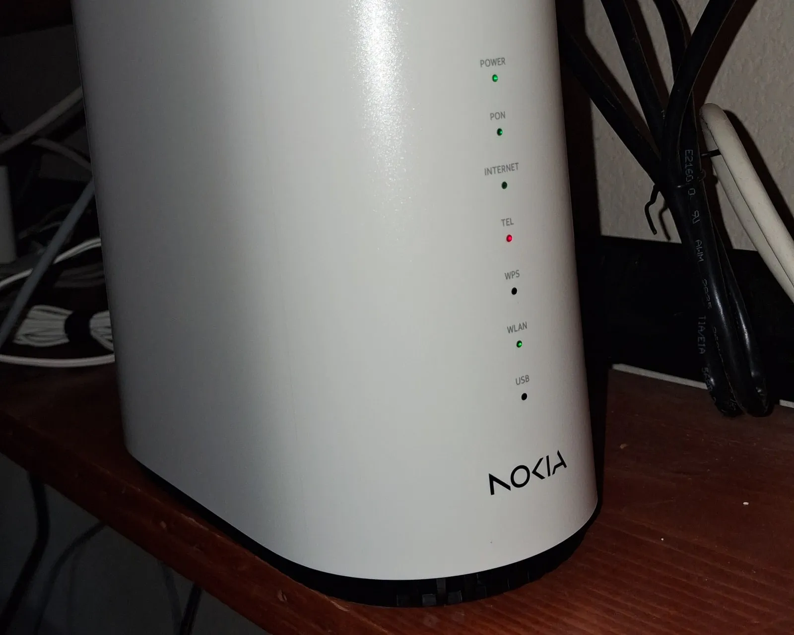 A white Nokia fiber gateway on a wooden shelf at home, with green lights labelled Power, PON, Internet and WLAN, a red Tel light, and black cables behind it.