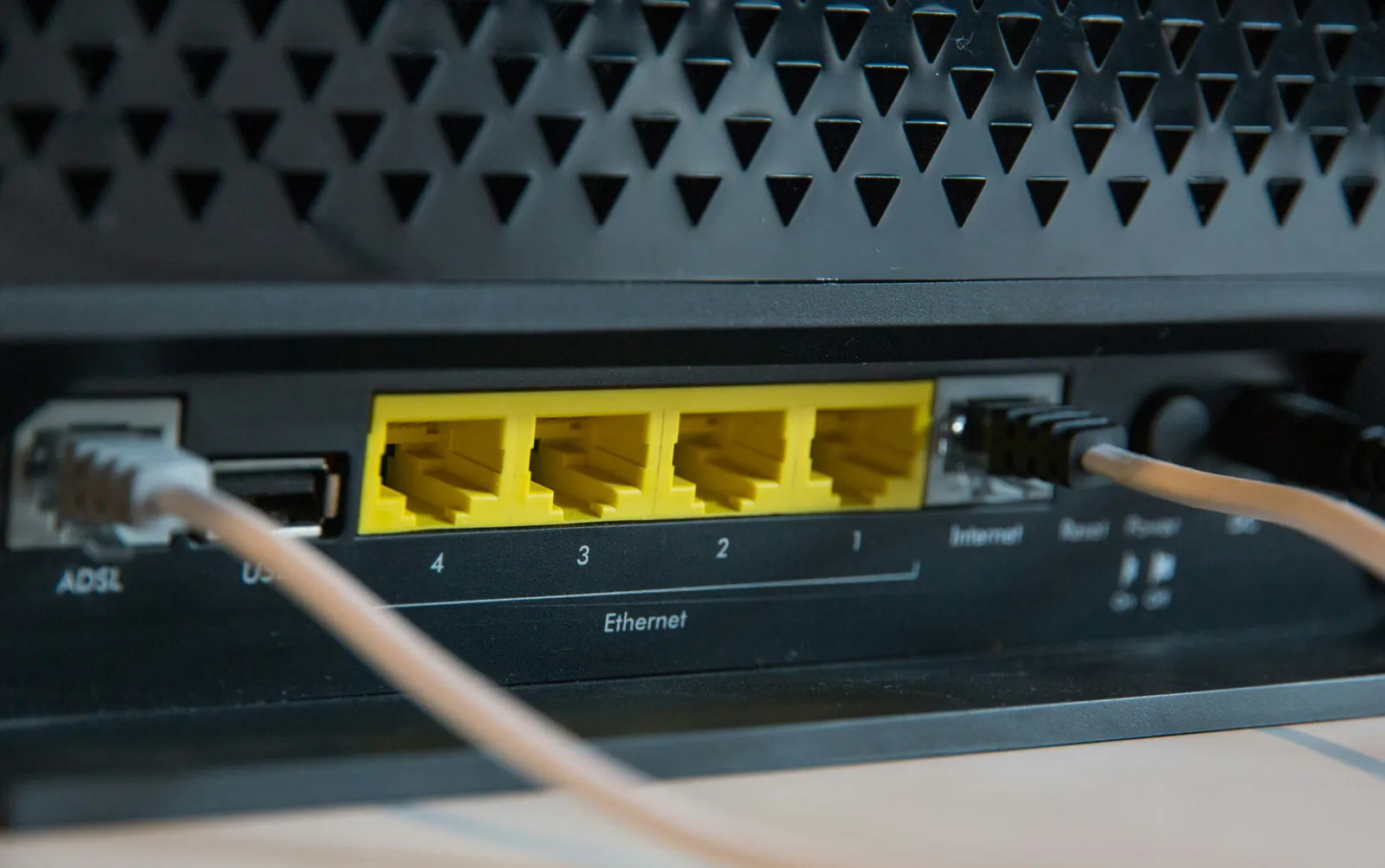 Close-up of the back of a black modem-router: a cable plugged into the socket labelled ADSL, a USB port, four yellow Ethernet ports numbered 4 to 1, and a cable in the port labelled Internet.
