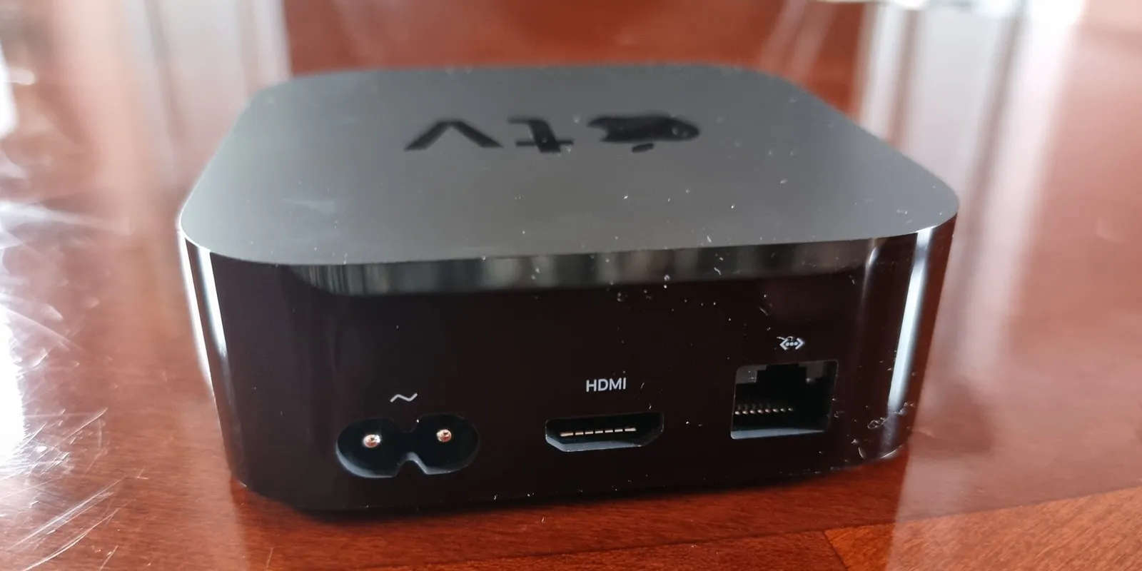 The back of a black Apple TV box on a wooden table, showing a power socket, an HDMI port and an Ethernet port.