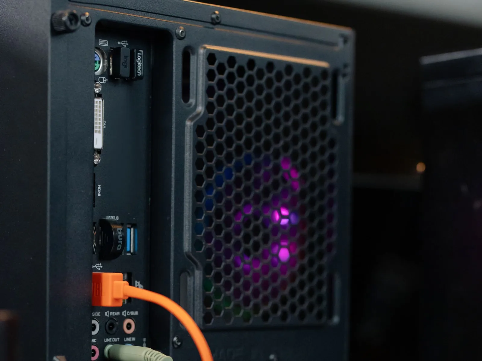 The back of a black desktop PC: an orange Ethernet cable is plugged into the network port on the rear panel, below the USB ports, next to a fan grille lit purple from inside.